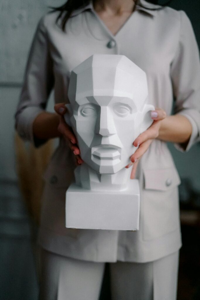 A woman in neutral attire holds a geometric sculpture bust indoors.