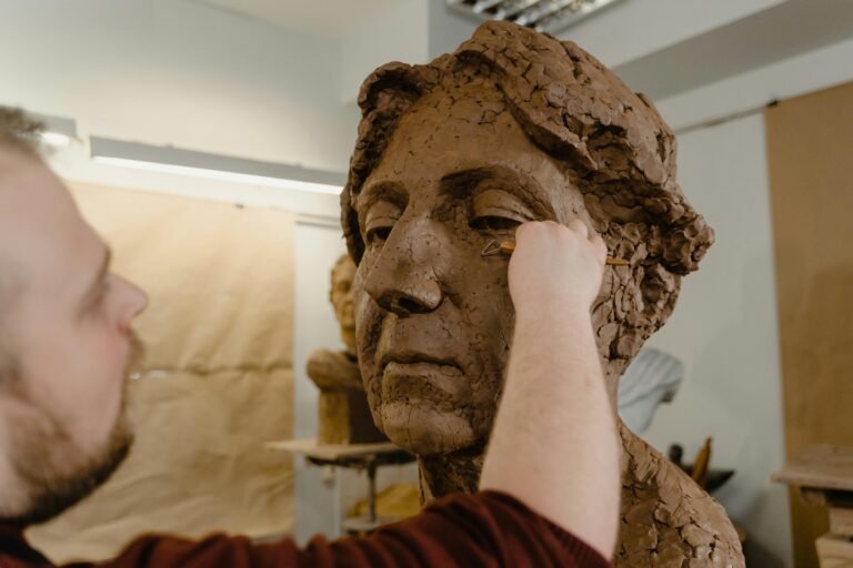 Artist shaping a clay bust with precision using a loop tool in a studio setting.